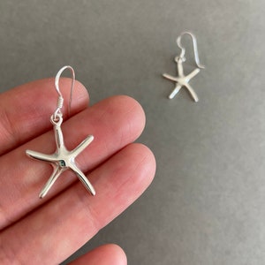 May include: A pair of silver starfish dangle earrings. The earrings are made of sterling silver and have a simple, elegant design.