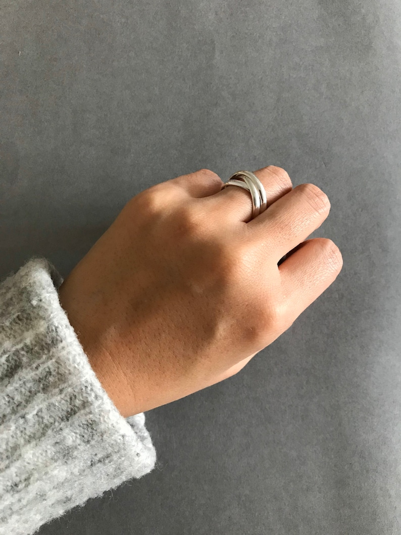 May include: A silver ring with a double band design. The ring is worn on the index finger of a hand.