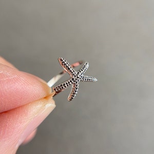May include: A silver ring with a starfish design. The starfish is textured and has a delicate, openwork design.