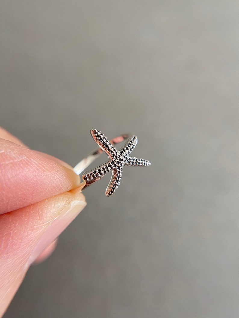 May include: A silver ring with a starfish design. The starfish is textured and has a delicate, openwork design.