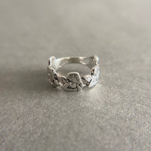 K&ouml;nnte beinhalten: Ein silberner Ring mit einem detaillierten Design aus ineinandergreifenden Bl&auml;ttern.