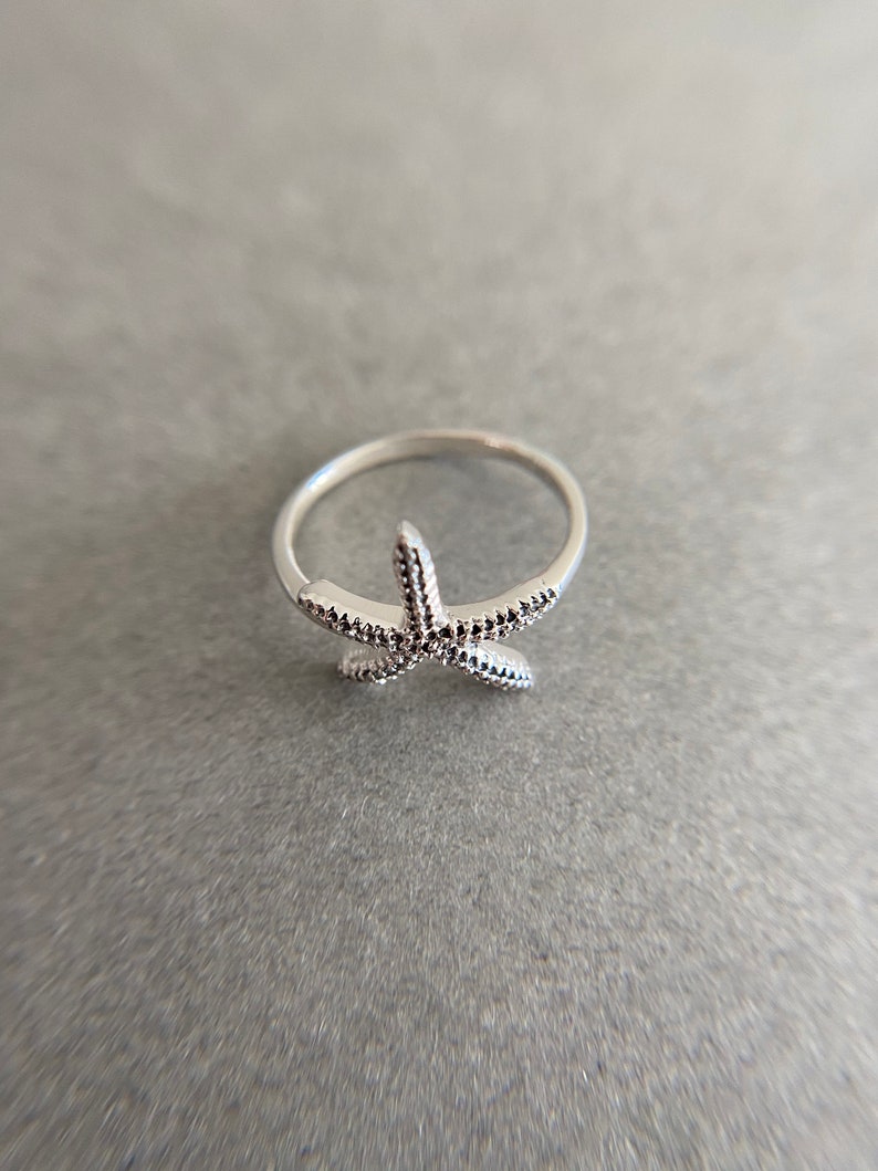 May include: A silver ring with a starfish design. The starfish is detailed with small dots.