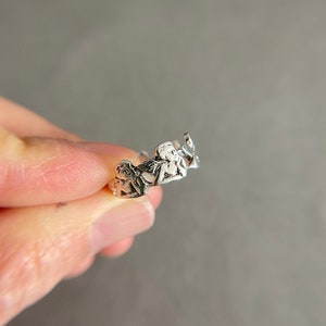 K&ouml;nnte beinhalten: Silberring mit einem Design aus drei Cherubinen, die sich an den H&auml;nden halten.