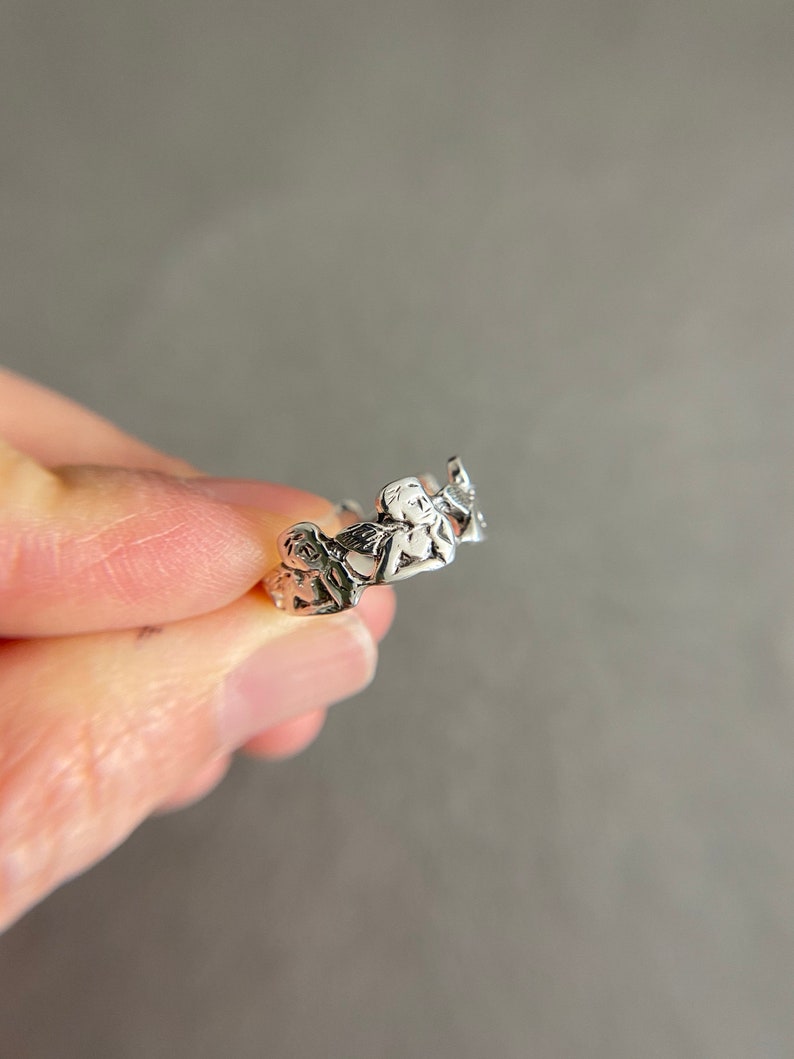 K&ouml;nnte beinhalten: Silberring mit einem Design aus drei Cherubinen, die sich an den H&auml;nden halten.