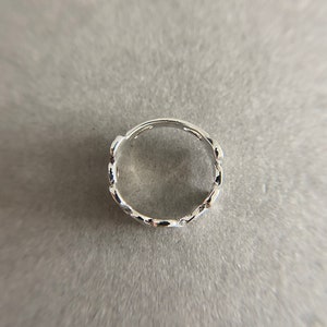 K&ouml;nnte beinhalten: Ein silberner Ring mit einem kettenartigen Design. Der Ring besteht aus kleinen, miteinander verbundenen ovalen Formen.