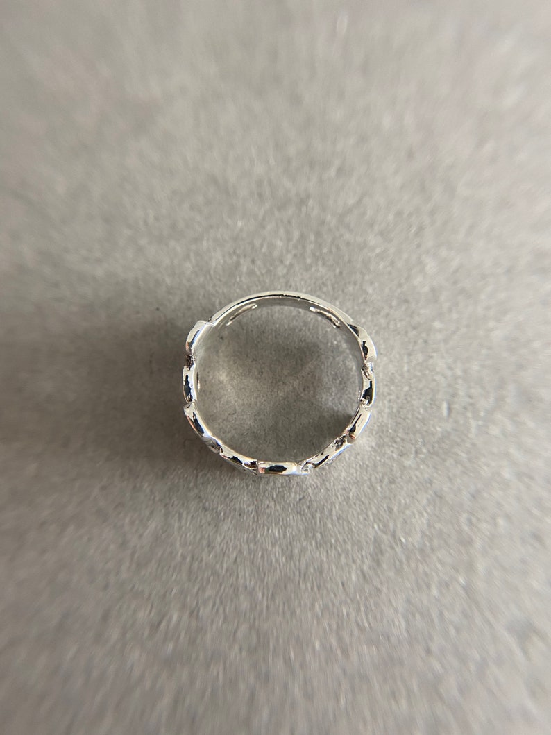 K&ouml;nnte beinhalten: Ein silberner Ring mit einem kettenartigen Design. Der Ring besteht aus kleinen, miteinander verbundenen ovalen Formen.