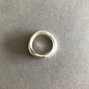 May include: A silver ring with a twisted design. The ring is made of two bands that are intertwined.