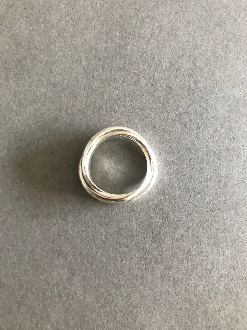 May include: A silver ring with a twisted design. The ring is made of two bands that are intertwined.