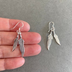 May include: A pair of silver dangle earrings with two feather charms on each earring.