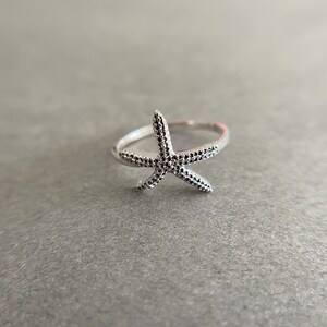 May include: A silver ring with a starfish design. The starfish is textured with small dots.