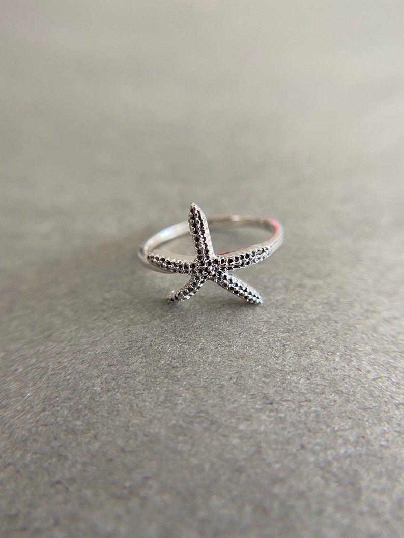 May include: A silver ring with a starfish design. The starfish is textured with small dots.