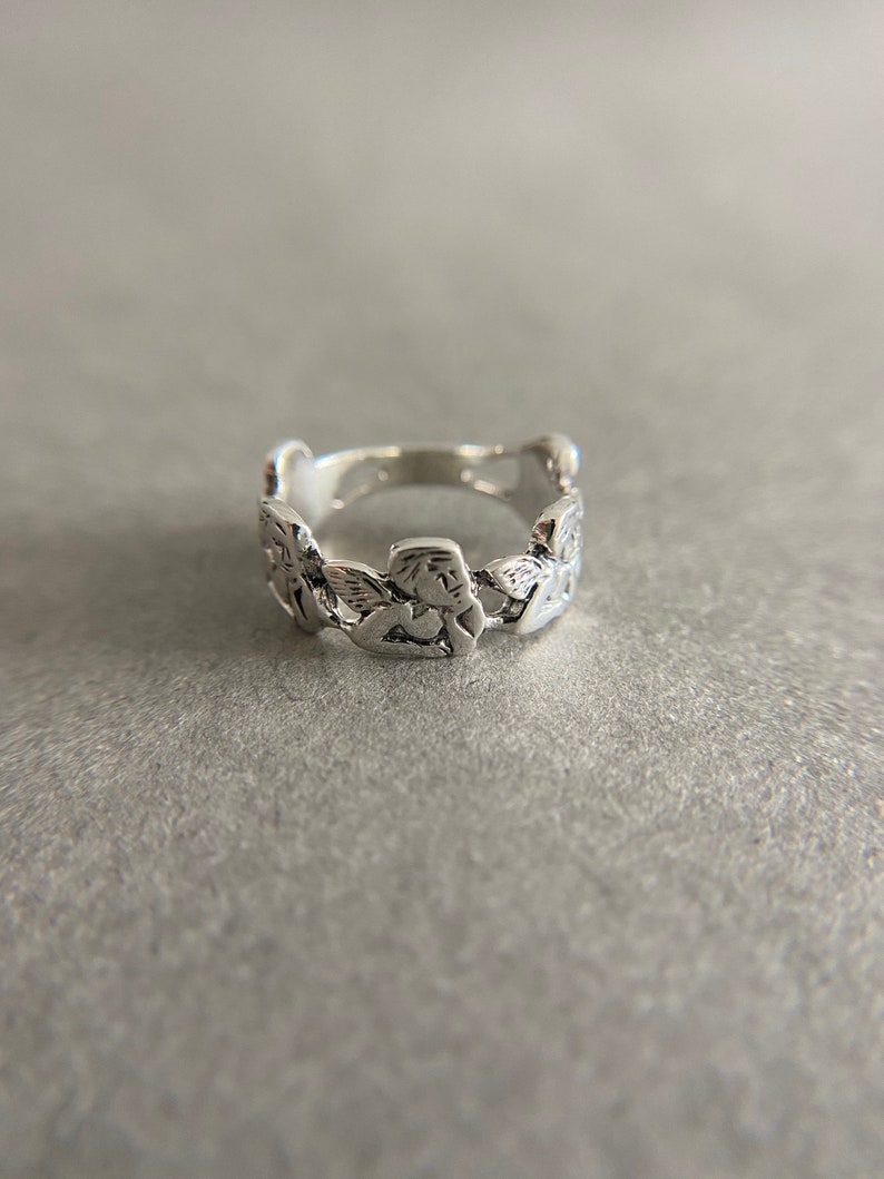 K&ouml;nnte beinhalten: Ein silberner Ring mit einem einzigartigen Design, das aus einer Reihe von verbundenen, strukturierten, blattartigen Formen besteht.