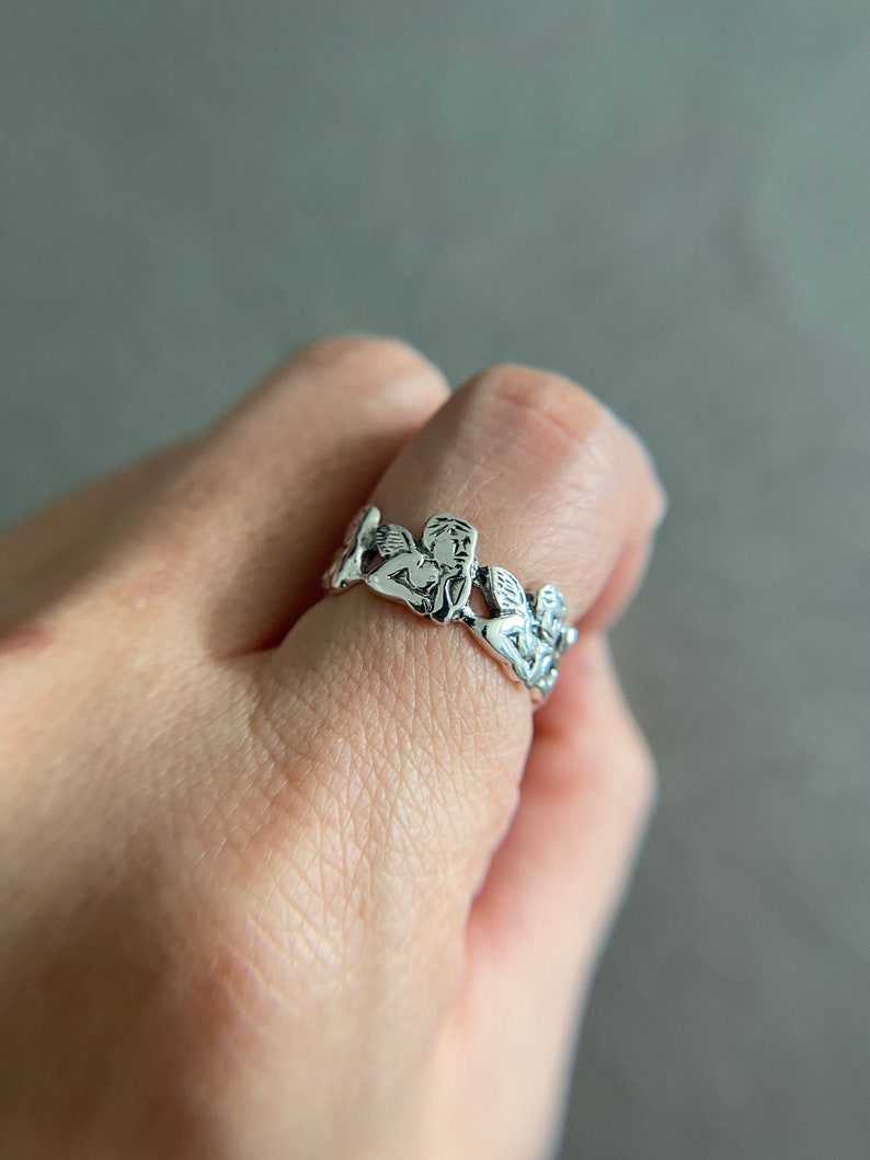 K&ouml;nnte beinhalten: Silberring mit einem Design aus mehreren Engeln, die sich an den H&auml;nden halten.