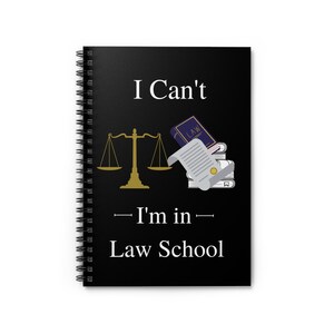 May include: Black spiral notebook with the text "I Can't - I'm in - Law School" in white. A gold scale of justice and a stack of books with a diploma are illustrated.