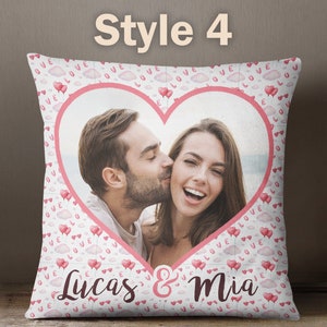 Puede incluir: Una almohada blanca con un marco en forma de coraz&oacute;n rosa que contiene una foto de una pareja. La almohada est&aacute; decorada con un patr&oacute;n rosa y blanco de nubes y corazones con las palabras "Love" impresas en ellos. El texto "Lucas & Mia" est&aacute; impreso en la parte inferior de la almohada.