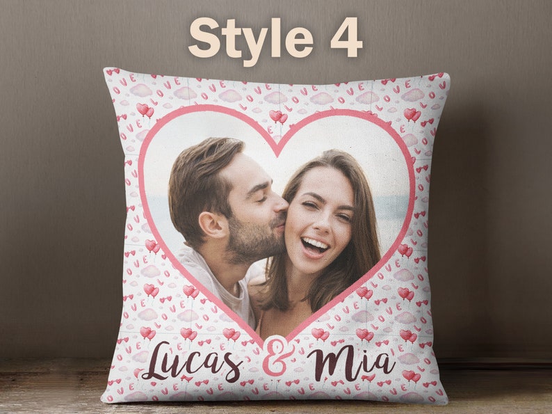Puede incluir: Una almohada blanca con un marco en forma de coraz&oacute;n rosa que contiene una foto de una pareja. La almohada est&aacute; decorada con un patr&oacute;n rosa y blanco de nubes y corazones con las palabras "Love" impresas en ellos. El texto "Lucas & Mia" est&aacute; impreso en la parte inferior de la almohada.