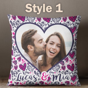 Puede incluir: Una almohada blanca con un marco de fotos en forma de coraz&oacute;n que presenta a una pareja. La almohada tiene un patr&oacute;n de corazones rosa y morado y las palabras "Love" y "Lucas & Mia".