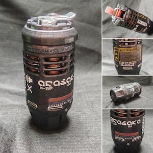 Könnte beinhalten: Ein schwarzes und silbernes zylindrisches Gerät mit dem Text "Arasaka" und "Concentrated Foam". Das Gerät hat einen silbernen Griff und ein Warnschild. Das Design umfasst kupferfarbene Spulen und eine rote Spitze.