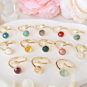 May include: A collection of 12 gold rings with different coloured gemstones. Each ring features a delicate leaf design on the band.