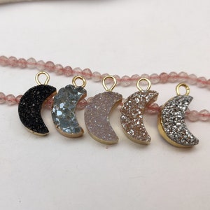 May include: Six gold-plated crescent moon charms with different coloured agate stones. The charms are strung on a pink beaded chain.