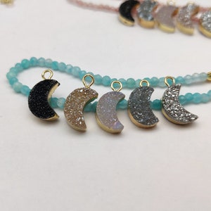 May include: A turquoise beaded bracelet with six crescent moon charms. The charms are made of different types of agate, including black, brown, white, and grey.