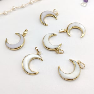 Pode incluir: Seis pingentes de lua crescente banhados a ouro com incrustações de madrepérola branca. Os pingentes medem aproximadamente 3,8 cm de comprimento.