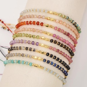 Puede incluir: Un conjunto de 12 pulseras delicadas con cuentas de piedras semipreciosas y separadores dorados. Las pulseras están superpuestas en la muñeca de una persona, mostrando un arcoíris de colores.