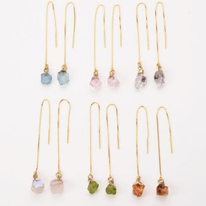 Könnte beinhalten: Sechs Paar goldene Ohrringe mit verschiedenen farbigen Edelstein-Tropfen. Die Edelsteine sind blau, rosa, grün und braun.