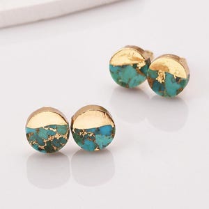 May include: A pair of circular stud earrings featuring a split design. The top half of each earring is smooth polished gold, while the bottom half consists of turquoise stone with natural dark veining and embedded gold-colored flecks.