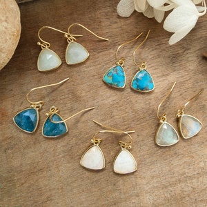 May include: Six pairs of gold triangle earrings with different gemstone colors. The earrings feature a variety of colors including white, blue, and turquoise.