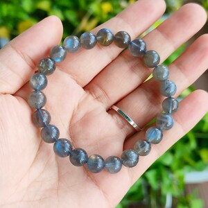 May include: A bracelet made of round, dark gray labradorite beads. The bracelet is on a person's hand.