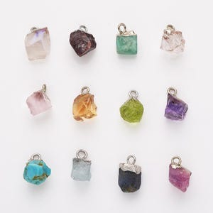 Pode incluir: Doze pingentes de pedras preciosas diferentes, cada um com uma argola de prata. As pedras preciosas são: ametista, citrino, esmeralda, água-marinha, rubi, safira, quartzo rosa, quartzo transparente, turquesa, granada, peridoto e ametista.