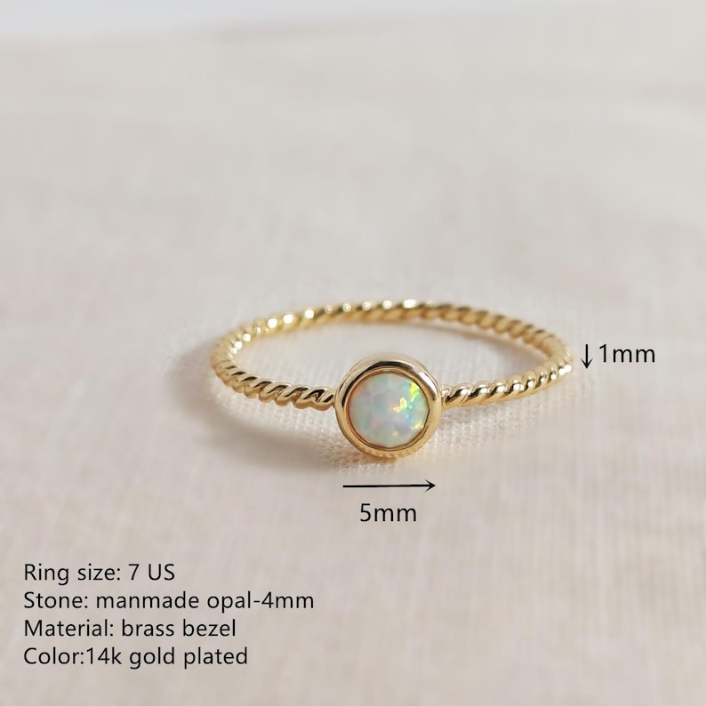 Puede incluir: Un anillo chapado en oro con una banda trenzada y una piedra de &oacute;palo artificial engastada de 5mm. La banda tiene un grosor de 1mm. El texto en la imagen especifica: Ring size: 7 US, Stone: manmade opal-4mm, Material: brass bezel, Color: 14k gold plated.