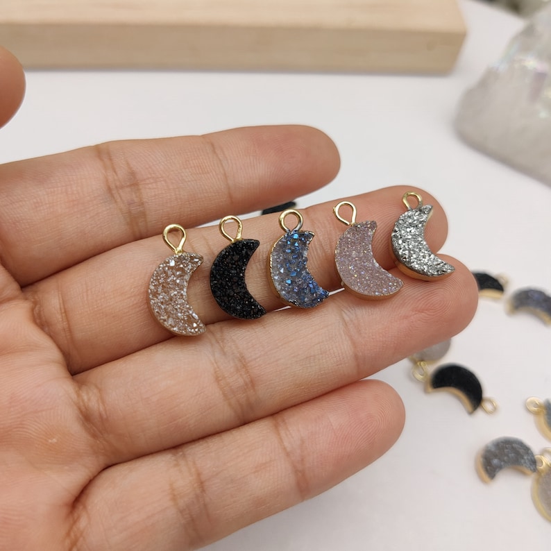 May include: Assortment of six gold-plated crescent moon charms with a glittery finish. The charms are available in black, blue, pink, and silver.