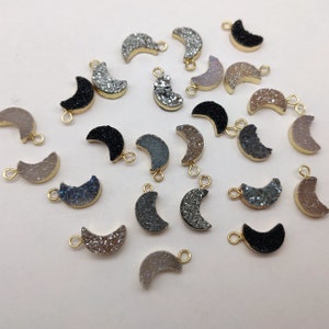May include: Assortment of 20 crescent moon shaped agate gemstone charms with gold jump rings. The charms are in various colours including black, grey, white, and brown.