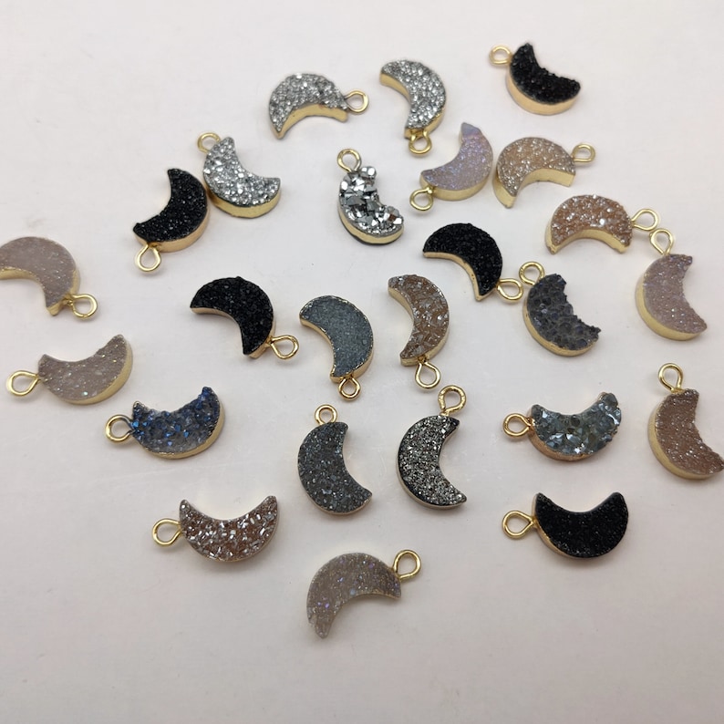 May include: Assortment of 20 crescent moon shaped agate gemstone charms with gold jump rings. The charms are in various colours including black, grey, white, and brown.