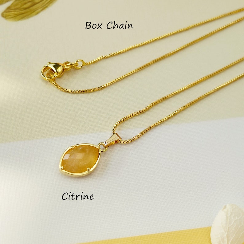 May include: A gold chain necklace with a citrine pendant. The chain is a box chain style. The pendant is a teardrop shape with a smooth, polished surface.