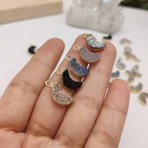 May include: Assortment of six crescent moon shaped charms with gold jump rings. The charms are made of agate and come in a variety of colours, including black, blue, grey, and white.