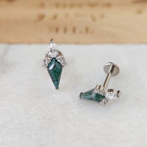 May include: Two silver-toned ear studs. Each stud features a green, diamond-shaped stone, accented with clear, round and pear-shaped crystals. The studs are designed for ear piercings and have a flat back.