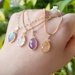 May include: Four gold necklaces with different colored gemstone pendants. The pendants are all in the shape of a teardrop and have a faceted design. The gemstones are a light blue, white, purple, and orange.