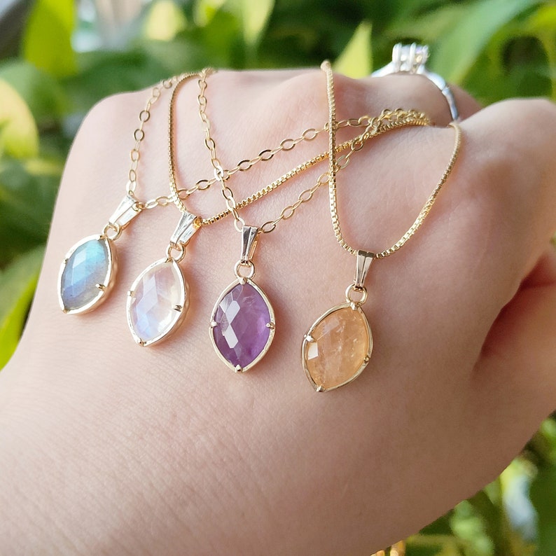 May include: Four gold necklaces with different colored gemstone pendants. The pendants are all in the shape of a teardrop and have a faceted design. The gemstones are a light blue, white, purple, and orange.
