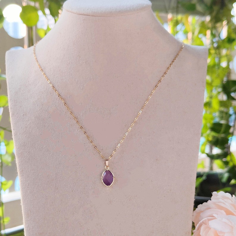 May include: A gold chain necklace with a purple gemstone pendant. The pendant is a faceted oval shape.
