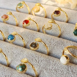 May include: A collection of gold rings with different coloured gemstones and leaf accents. The rings are displayed in a velvet-lined box.