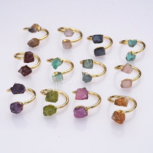 May include: Twelve gold rings with different colored gemstones. Each ring has two gemstones, one on each side of the band.