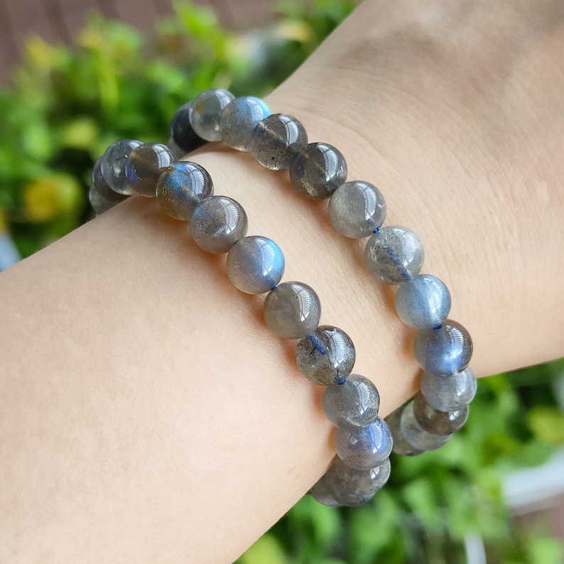 May include: Two beaded bracelets made of iridescent blue-grey labradorite stones. The bracelets are stacked on a person's wrist.