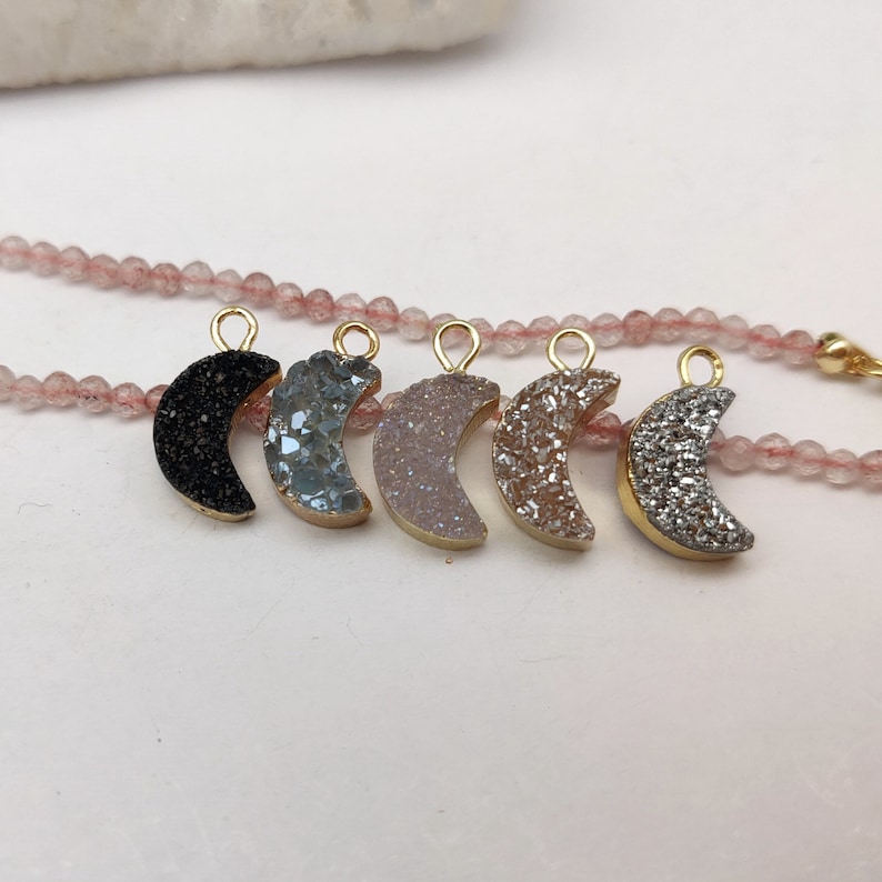 May include: Six gold-plated crescent moon charms with different coloured agate stones. The charms are strung on a pink beaded chain.