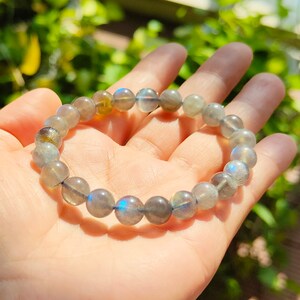 May include: A gray labradorite gemstone bracelet with iridescent blue and green hues. The bracelet is made of round beads and is strung on a clear elastic cord.