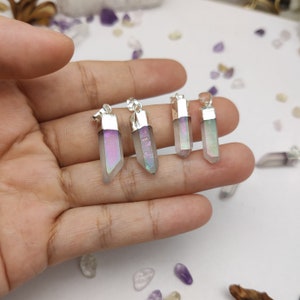 May include: Four iridescent crystal pendants with silver settings. The crystals are clear with a rainbow sheen. The pendants are arranged in a row on a hand.