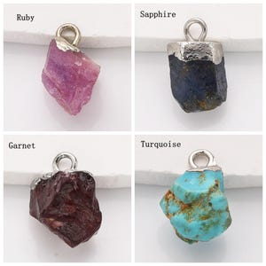 May include: Four gemstone pendants with silver bail loops. The gemstones are ruby, sapphire, garnet, and turquoise.