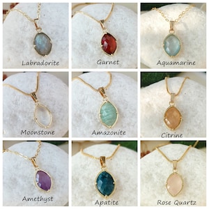 May include: Nine gold necklaces with different gemstone pendants. The gemstones are labradorite, garnet, aquamarine, moonstone, amazonite, citrine, amethyst, apatite, and rose quartz.